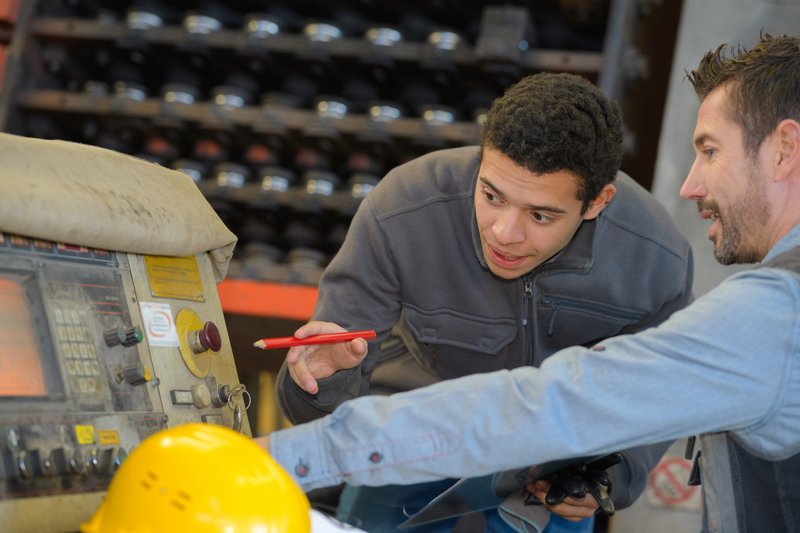 A photo of a youth apprentice discussing a piece of equipment with a mentor